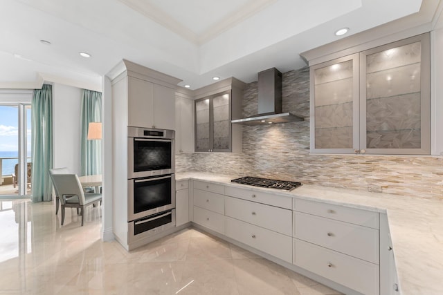 kitchen with glass insert cabinets, decorative backsplash, appliances with stainless steel finishes, wall chimney exhaust hood, and a warming drawer