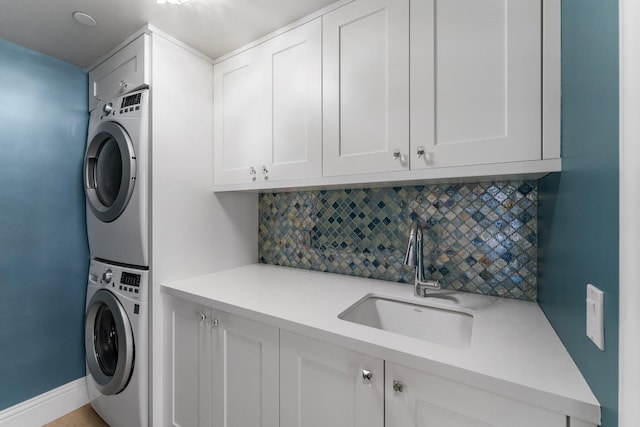 clothes washing area with a sink, stacked washer / drying machine, cabinet space, and baseboards