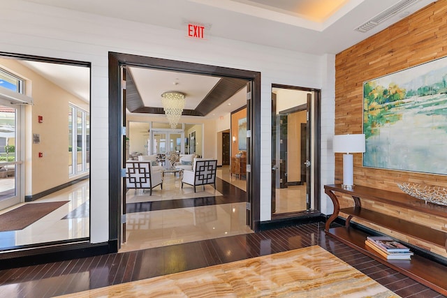 hall featuring a tray ceiling, wood finished floors, visible vents, and a chandelier