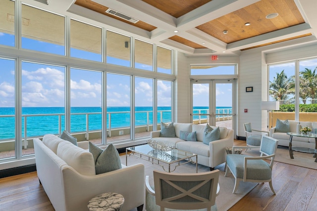 living area featuring visible vents, light wood finished floors, coffered ceiling, a water view, and a towering ceiling