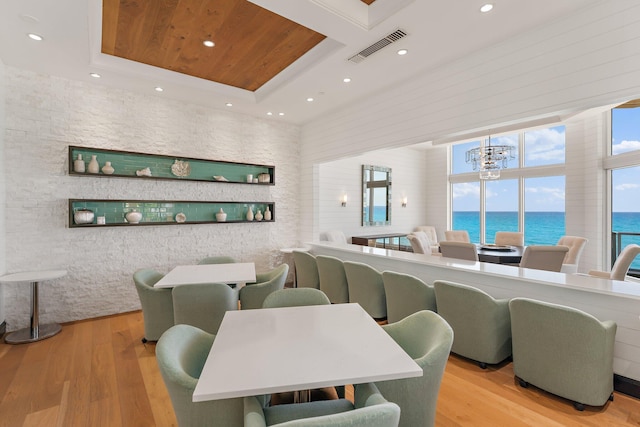 dining space featuring visible vents, wood finished floors, a raised ceiling, and a water view