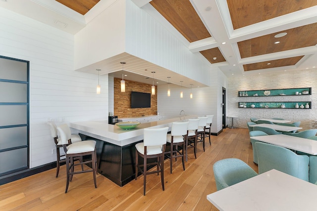 kitchen featuring open floor plan, a breakfast bar, beam ceiling, light wood-style floors, and coffered ceiling