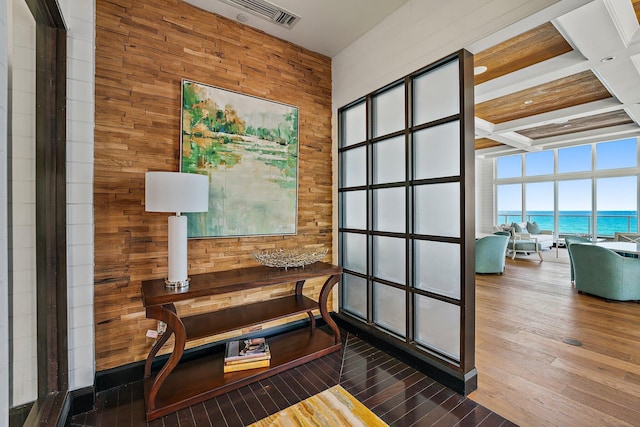 home office with visible vents, a water view, wood walls, wood finished floors, and coffered ceiling