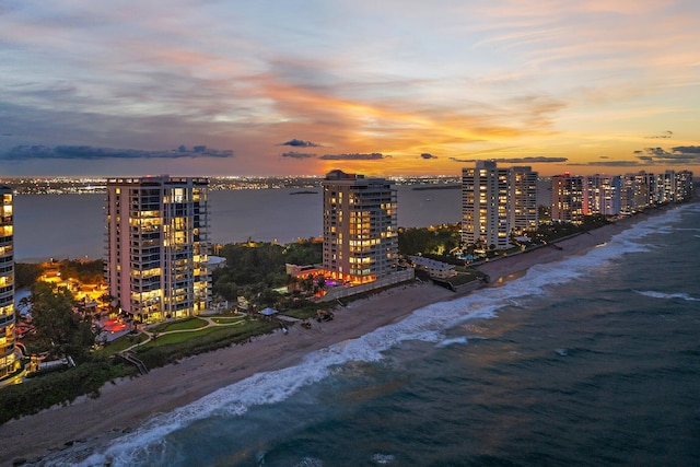 aerial view at dusk featuring a city view, a view of the beach, and a water view