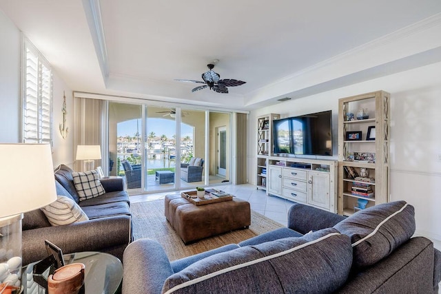 living area with light tile patterned floors, crown molding, a raised ceiling, and a ceiling fan