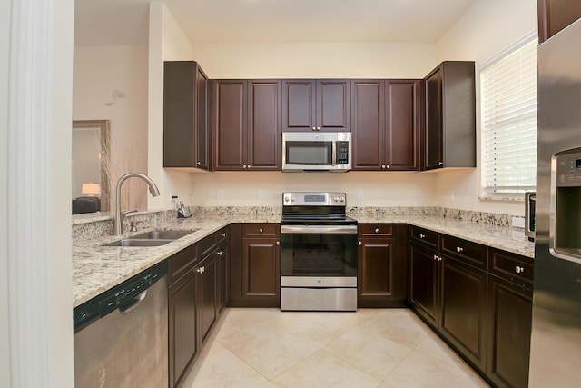 kitchen featuring a sink, stainless steel appliances, light stone countertops, and dark brown cabinets