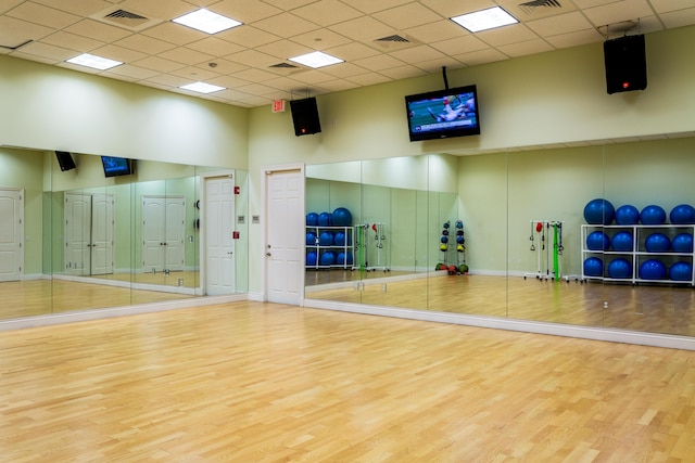 exercise area with a high ceiling, wood finished floors, visible vents, and a paneled ceiling