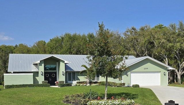 view of front facade with stucco siding, a front lawn, concrete driveway, an attached garage, and metal roof