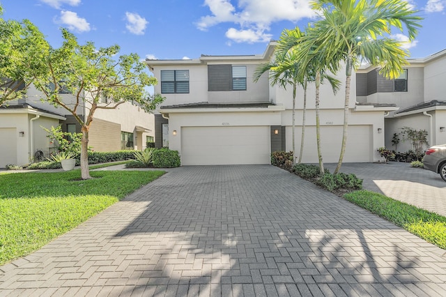 view of property with a front yard, decorative driveway, an attached garage, and stucco siding