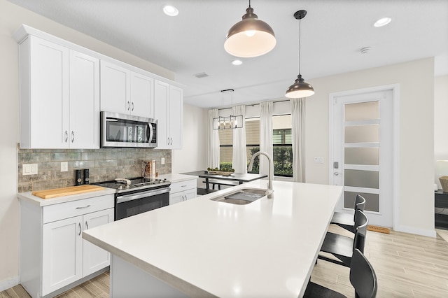 kitchen with a kitchen island with sink, a sink, decorative backsplash, light countertops, and appliances with stainless steel finishes