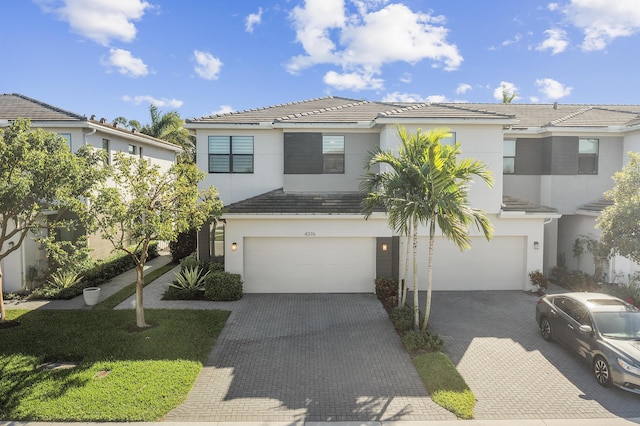 view of front facade with decorative driveway, a garage, stucco siding, and a tiled roof