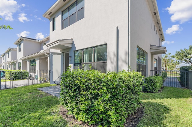 view of side of property with stucco siding, a lawn, and fence