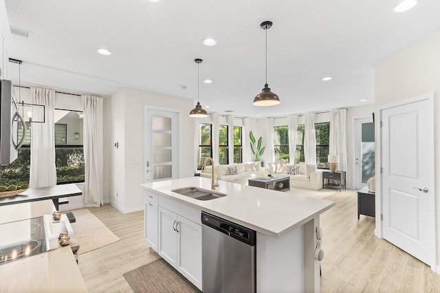 kitchen featuring light wood-style flooring, a sink, open floor plan, appliances with stainless steel finishes, and light countertops