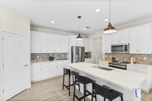 kitchen with a sink, light countertops, appliances with stainless steel finishes, white cabinetry, and decorative light fixtures