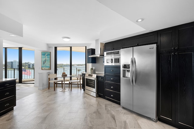 kitchen with a wealth of natural light, stainless steel appliances, wall chimney exhaust hood, and dark cabinets