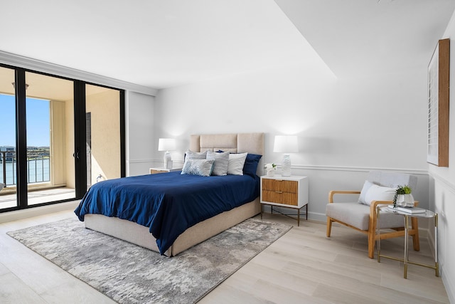 bedroom with baseboards, wood finished floors, floor to ceiling windows, and access to exterior