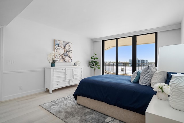 bedroom featuring access to exterior, baseboards, a wall of windows, and light wood-style floors