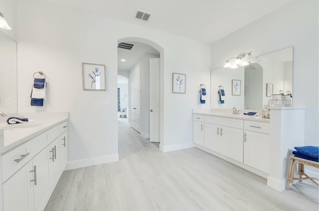 bathroom featuring a sink, baseboards, two vanities, and wood finished floors