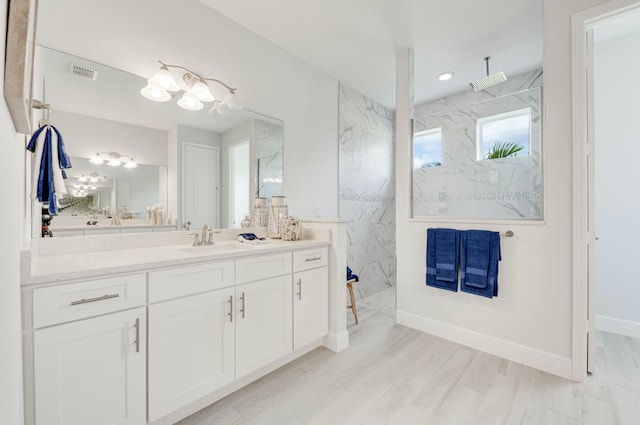 full bath with a marble finish shower, visible vents, baseboards, wood finished floors, and vanity