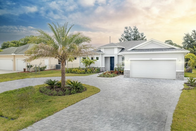 view of front of home with stucco siding, stone siding, curved driveway, a front yard, and a garage