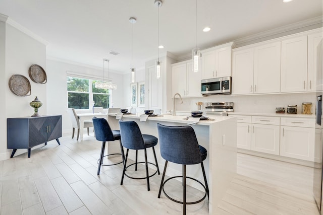 kitchen featuring ornamental molding, an island with sink, backsplash, appliances with stainless steel finishes, and light countertops