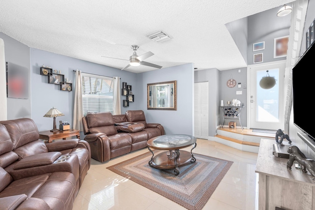 living room featuring ceiling fan, light tile patterned floors, visible vents, and a textured ceiling