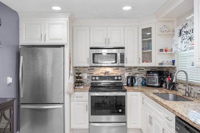 kitchen with a sink, stainless steel appliances, white cabinets, glass insert cabinets, and light stone countertops