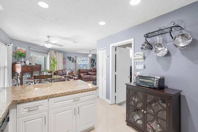 kitchen featuring light stone counters, light tile patterned floors, a ceiling fan, white cabinets, and a textured ceiling