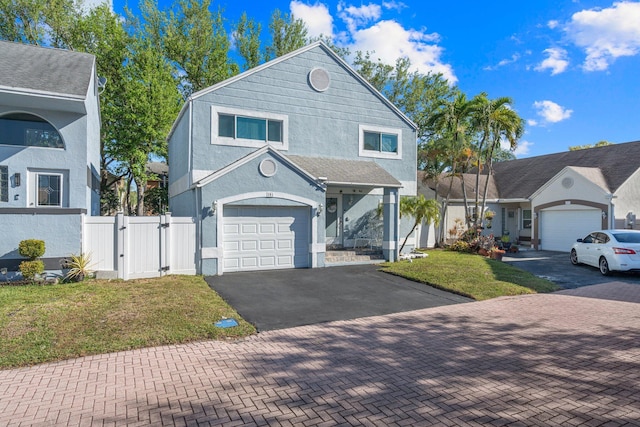 view of front facade with a front yard, a gate, an attached garage, stucco siding, and aphalt driveway