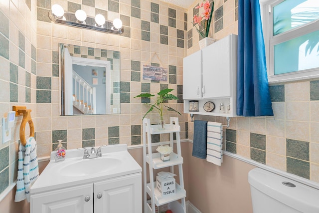 half bath with toilet, tile walls, and vanity