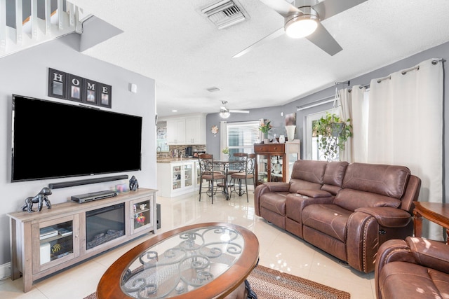 living area featuring light tile patterned floors, visible vents, a textured ceiling, and ceiling fan