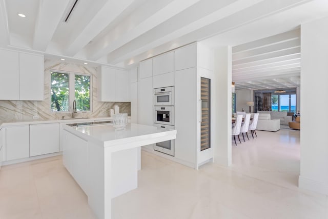 kitchen featuring a sink, light countertops, white cabinetry, beamed ceiling, and tasteful backsplash