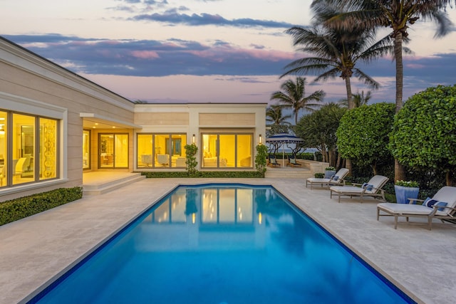 pool at dusk featuring a patio and an outdoor pool