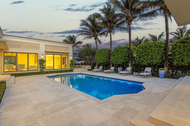 pool at dusk with an outdoor pool and a patio