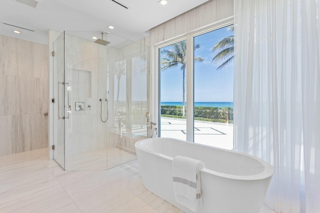 bathroom featuring recessed lighting, a marble finish shower, a water view, and a freestanding bath