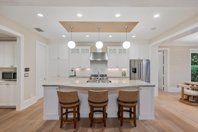 kitchen with visible vents, a kitchen island with sink, stainless steel appliances, decorative backsplash, and wall chimney range hood