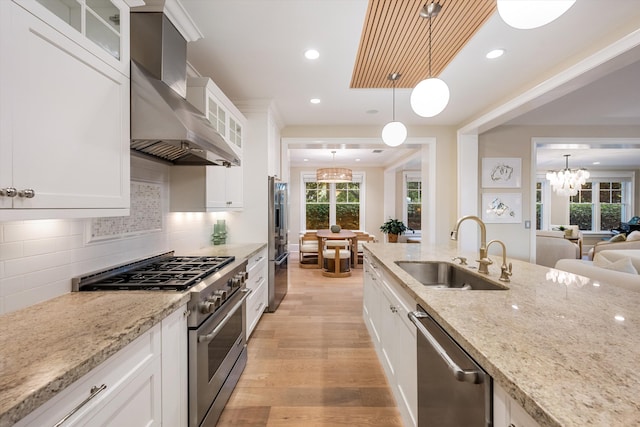 kitchen featuring wall chimney range hood, light wood-style floors, an inviting chandelier, high end appliances, and a sink