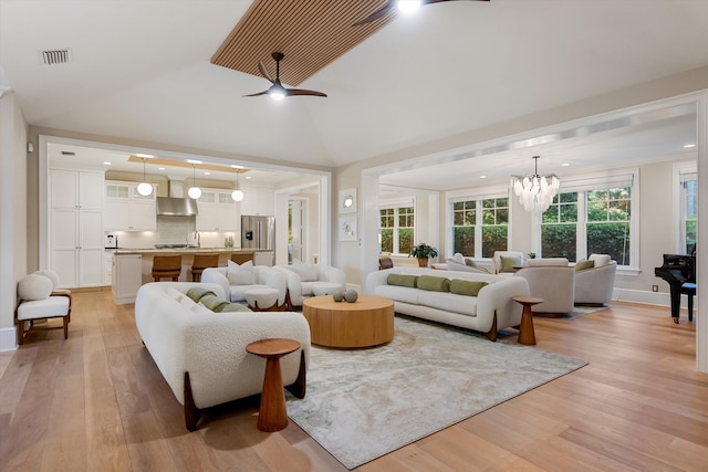 living room featuring visible vents, light wood-style flooring, ceiling fan with notable chandelier, and lofted ceiling