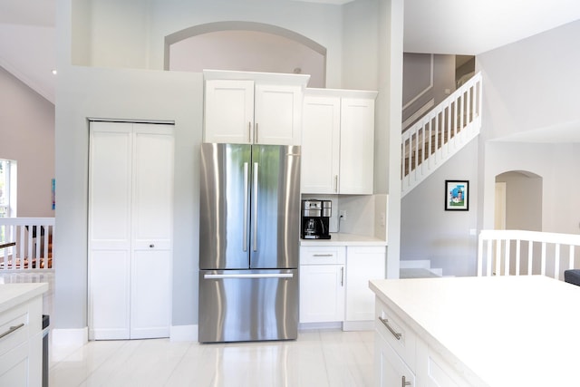 kitchen featuring white cabinetry, light countertops, freestanding refrigerator, and a towering ceiling