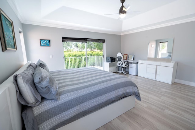 bedroom featuring multiple windows, a raised ceiling, light wood-style flooring, and access to outside