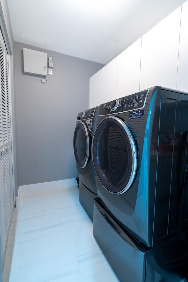 clothes washing area with light tile patterned floors, baseboards, cabinet space, and washing machine and clothes dryer