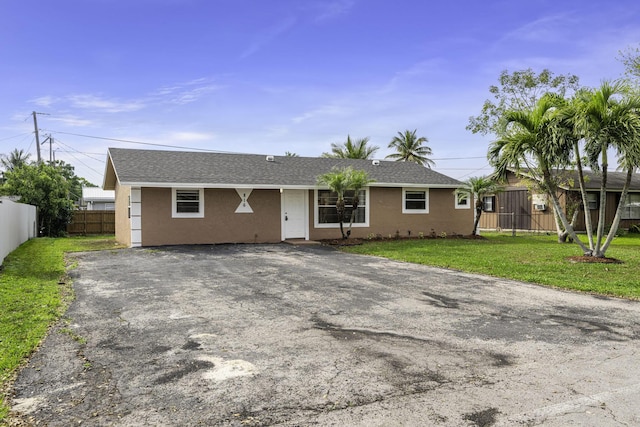 ranch-style house featuring stucco siding, aphalt driveway, a front yard, and fence