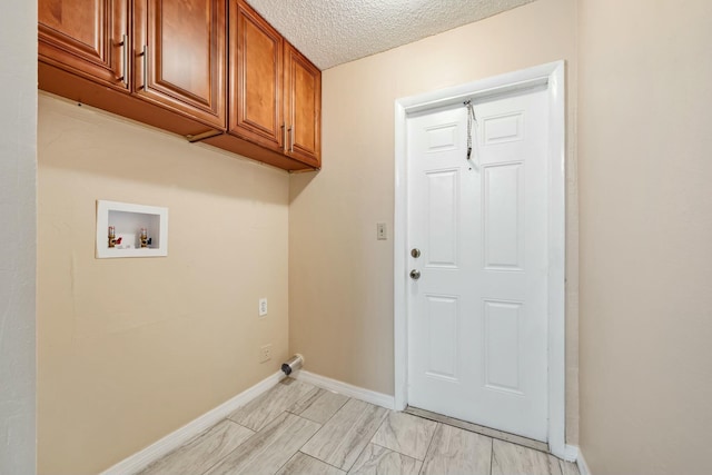 washroom featuring hookup for a washing machine, cabinet space, baseboards, and a textured ceiling