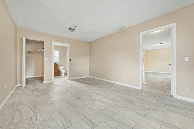 unfurnished bedroom with a spacious closet, baseboards, visible vents, and a textured ceiling