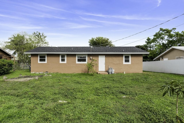 rear view of property featuring stucco siding, a lawn, and fence