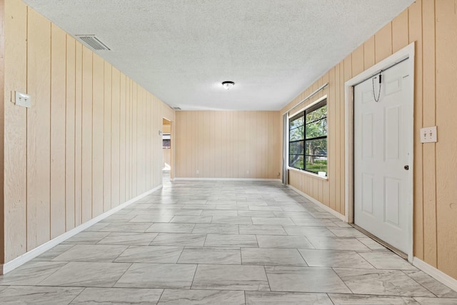 spare room featuring visible vents, baseboards, a textured ceiling, and wooden walls