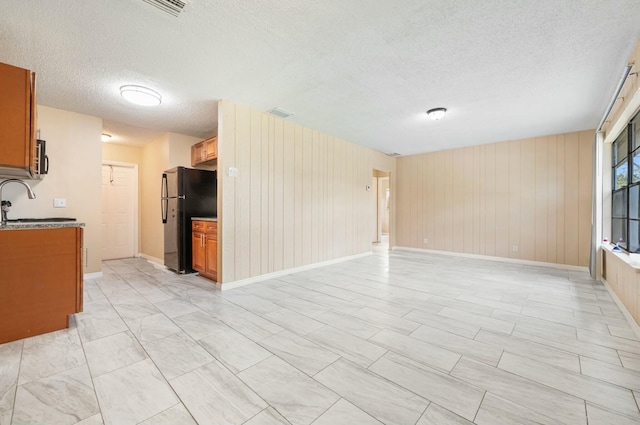 interior space featuring a sink, a textured ceiling, open floor plan, freestanding refrigerator, and brown cabinetry