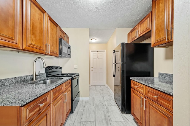 kitchen featuring brown cabinets, black appliances, a sink, dark stone countertops, and a textured ceiling