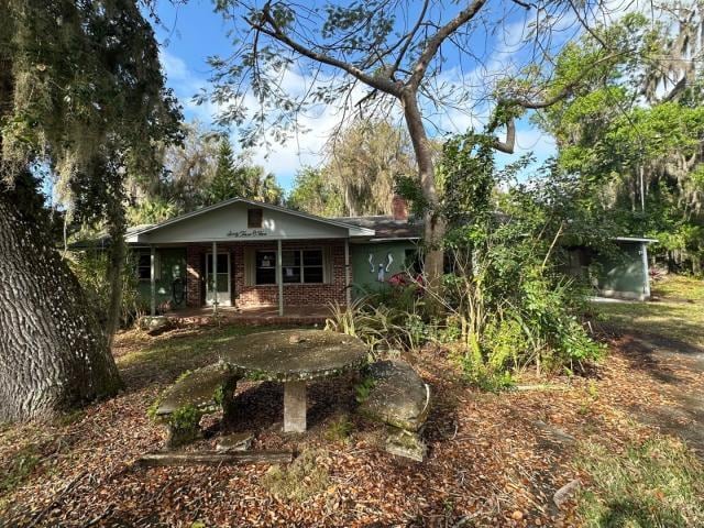 ranch-style home with a porch, brick siding, and a chimney