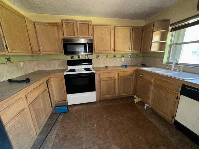 kitchen featuring stainless steel microwave, white dishwasher, electric range, a textured ceiling, and a sink